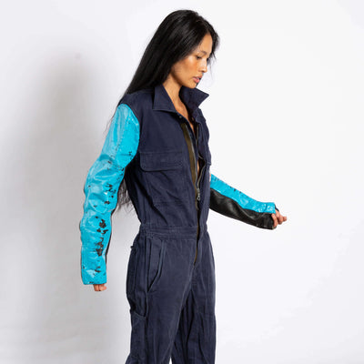 Model wears a jumpsuit that is dark navy blue and zipper up the front.  the sleeves are made of a different leather materials that is bright blue.  The paint is cracked showing black showing through.