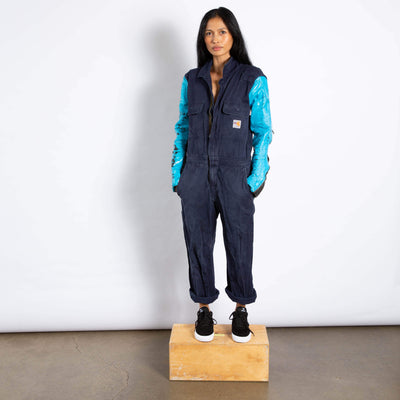 Model wears a jumpsuit that is dark navy blue and zupes up the front.  It has two pockets with flaps.  the sleeves are made of a different leather materials that is bright blue.  The paint is cracked showing black showing through.