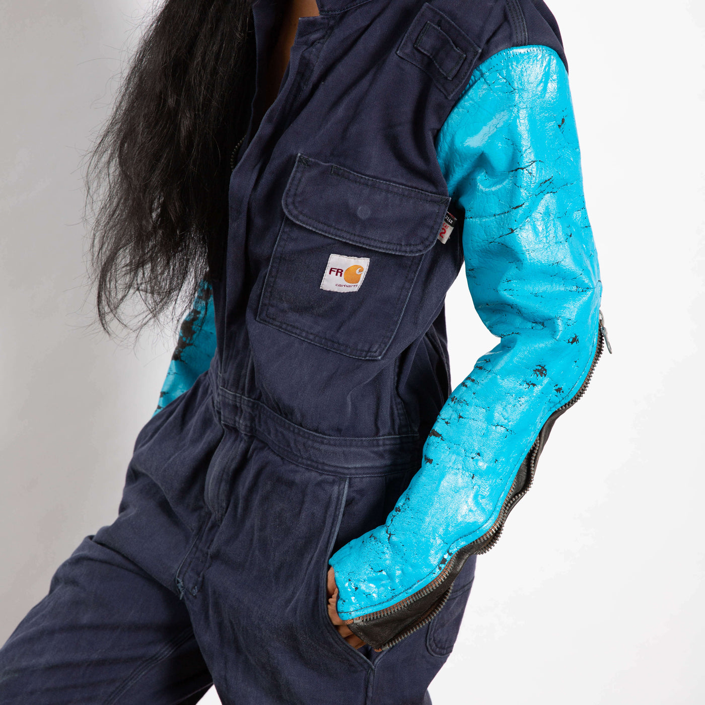Model wears a jumpsuit that is dark navy blue and zipper up the front.  the sleeves are made of a different leather materials that is bright blue.  The paint is cracked showing black showing through.