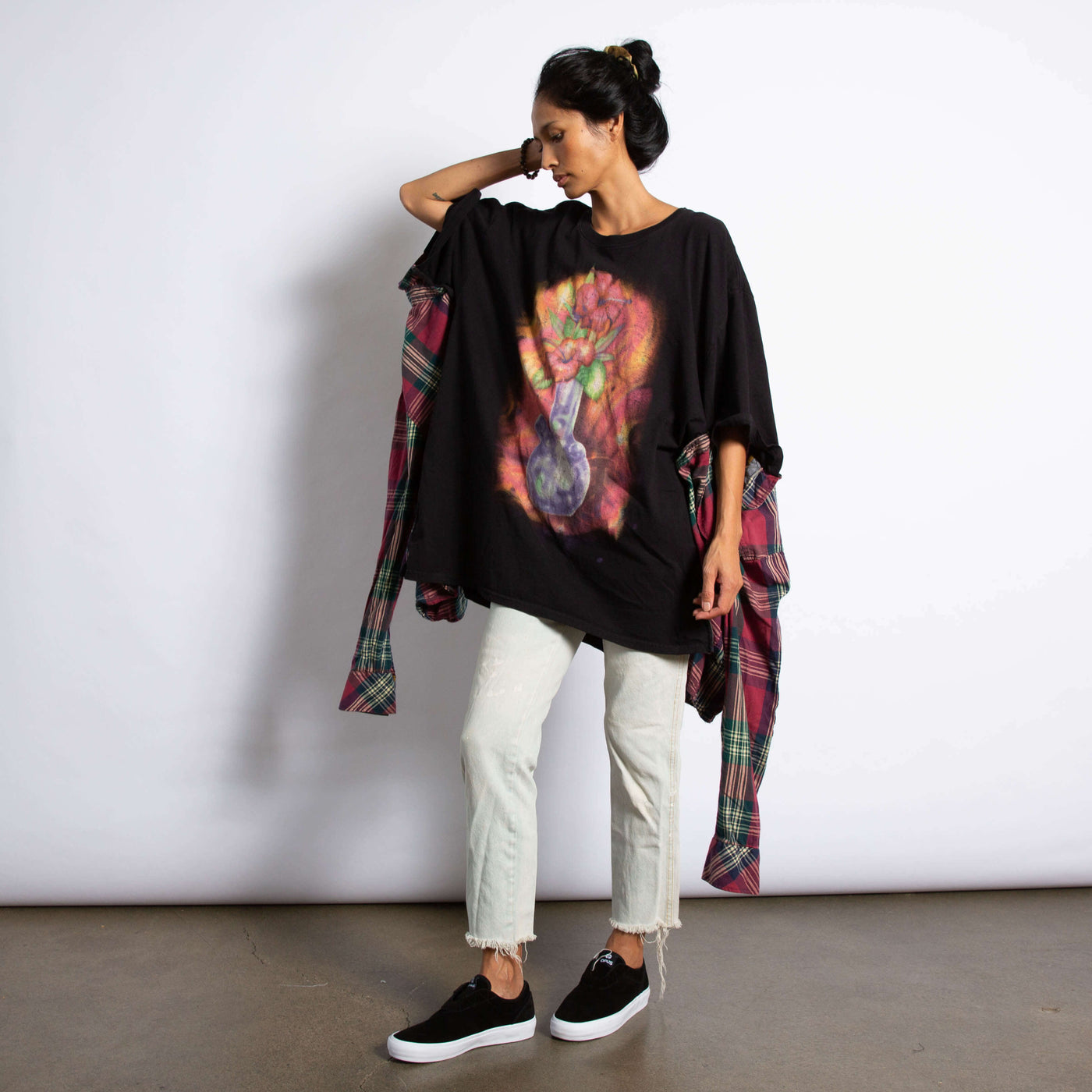 Model is wearing an oversized black Tee with a graphic of a glass bong with flowers. On the sides of the tee the sides of a flannel shirt are sewn on