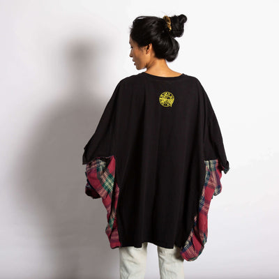 Model is wearing an oversized black Tee with a yellow logo that says Dries Van Noten and Stussy. On the sides of the tee the sides of a flannel shirt are sewn on.