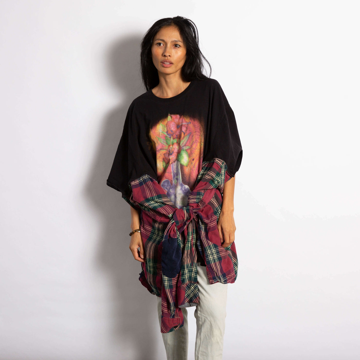 Model is wearing an oversized black Tee with a graphic of a glass bong with flowers. On the sides of the tee the sides of a flannel shirt are sewn on.  Sleeves are tied together at the waist.
