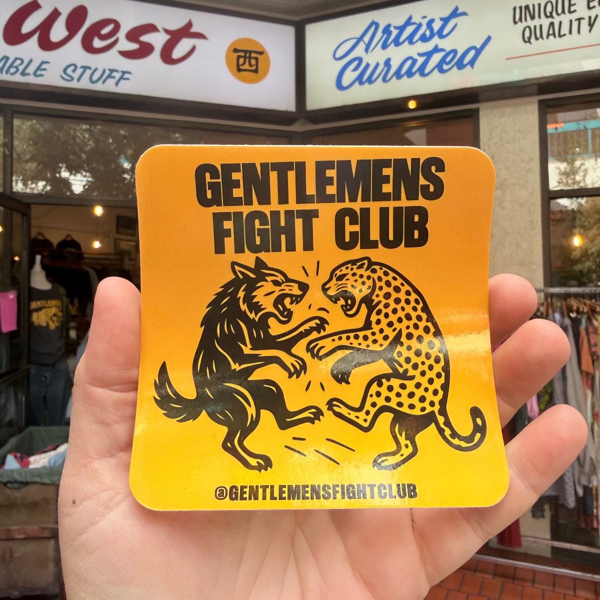 Hand holding a 'Gentlemen's Fight Club' sticker with store interior in the background