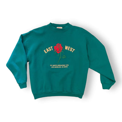 Emerald green sweatshirt on white background. The sweatshirt has a red rose embroidered on the center. To the left of the rose it says “EAST” and to the right it says “WEST” under the rose reads “ 727 NORTH BROADWAY #115 LOS ANGELES, CA 90012” in pink text.