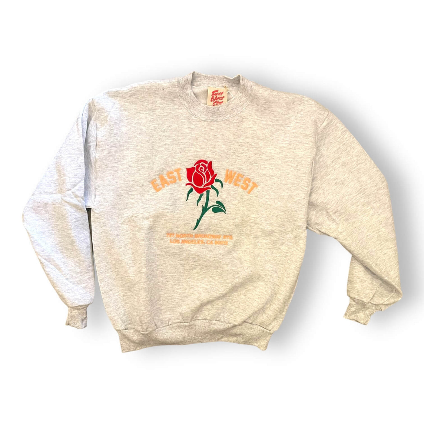 Light speckled Heather grey sweatshirt on white background. The sweatshirt has a red rose embroidered on the center. To the left of the rose it says “EAST” and to the right it says “WEST” under the rose reads “ 727 NORTH BROADWAY #115 LOS ANGELES, CA 90012” in pink text.