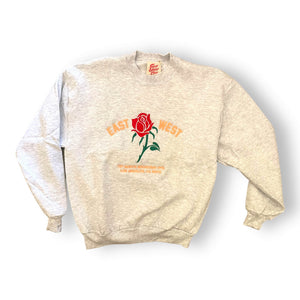 Light speckled Heather grey sweatshirt on white background. The sweatshirt has a red rose embroidered on the center. To the left of the rose it says “EAST” and to the right it says “WEST” under the rose reads “ 727 NORTH BROADWAY #115 LOS ANGELES, CA 90012” in pink text.