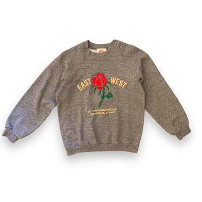 Dark heather grey sweatshirt on white background, sweatshirt has a red rose embroidered on the center with text “ EAST WEST” with the rose in the middle and “727 North Broadway #115 Los Angeles CA 90012” below.