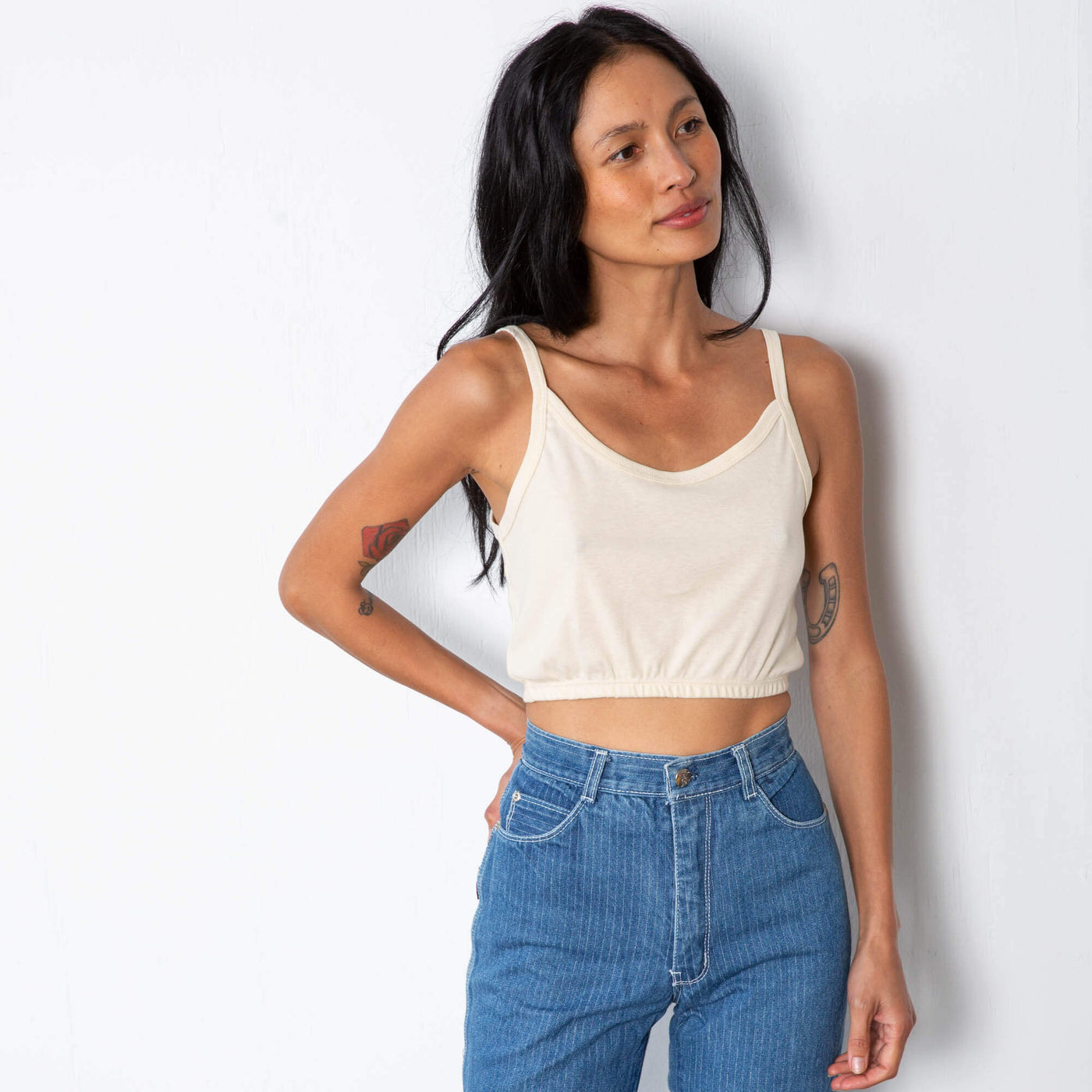 Jade is wearing a natural colored tank top with thin straps and elastic on the hem.  Worn with high waisted denim.