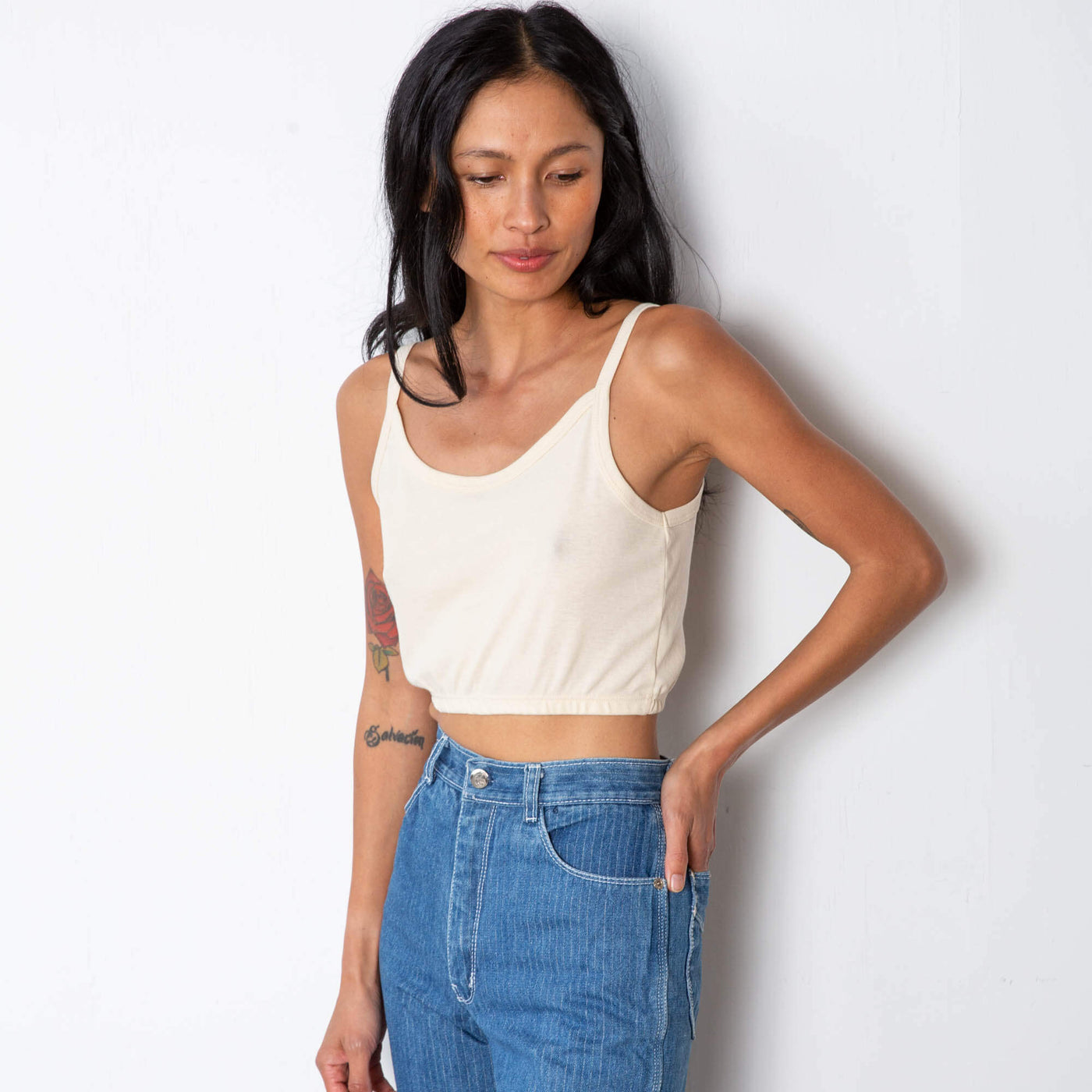 Jade is wearing a natural colored tank top with thin straps and elastic on the hem.  Worn with high waisted denim.